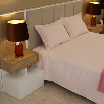 Cama com cabeceira estofada e roupa de cama rosa claro, mesas de cabeceira flutuantes com candeeiros de vidro âmbar e abajures castanhos.