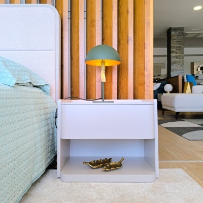 Mesa de cabeceira branca com candeeiro verde e objectos dourados numa sala com parede de madeira e cama azul claro