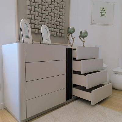 Cômoda cinza claro com gavetas abertas e objetos decorativos em cima junto a parede branca com quadro elétrico