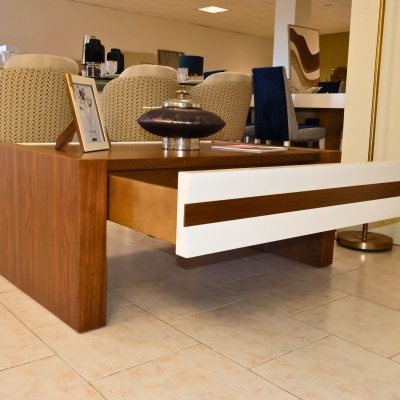 Mesa de centro de madeira com gaveta branca e jarra metálica em ambiente com cadeiras estofadas coloridas