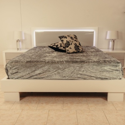 Cama de casal branca com luzes LED, coberta cinzenta e almofadas decorativas em quarto com mesas de cabeceira e planta
