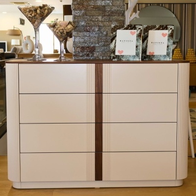 Cómoda branca com detalhes em madeira, copos decorativos cheios de conchas e quadros decorativos com texto BATISTA.