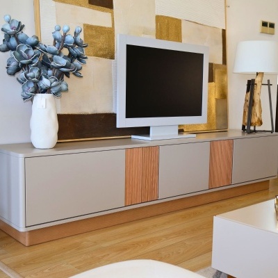 Móvel de TV cinzento com detalhes em madeira e televisão com flores azuis num vaso branco e candeeiro com abajur branco