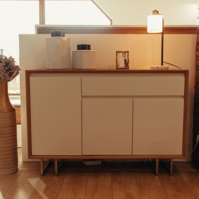 Aparador moderno em madeira com portas brancas, decorado com frascos, moldura e candeeiro