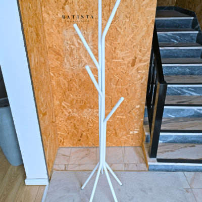 Cabideiro branco em metal com design de árvore contra parede de madeira OSB junto a escada interior.