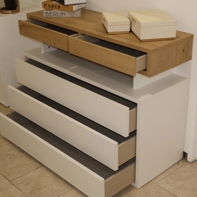 Cómoda branca com gavetas abertas e caixas creme em cima