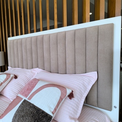 Cabeceira estofada bege com almofadas rosa e branco em cama, divisória de madeira ao fundo