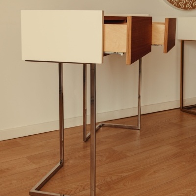 Secretária de madeira clara, tampo creme e pernas metálicas cromadas num ambiente interior.