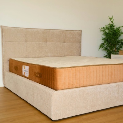 Cama estofada bege com colchão castanho e planta decorativa