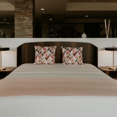 Cama de casal com cabeceira em madeira escura, almofadas coloridas e mesas de cabeceira com candeeiros