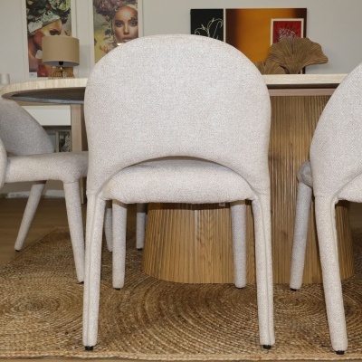 Cadeiras estofadas bege em volta de mesa de madeira com quadro ao fundo.