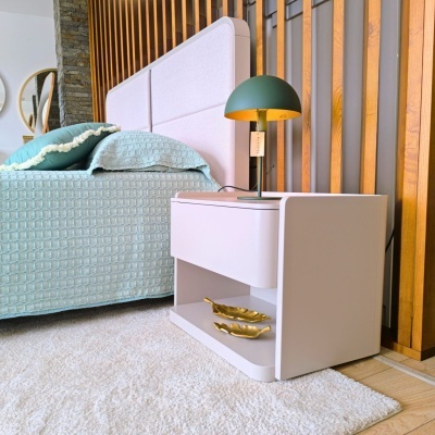 Mesa de cabeceira branca com candeeiro verde ao lado de cama com cabeceira rosa e roupa de cama azul clara