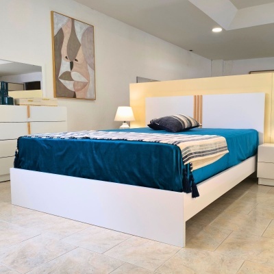 Quarto com cama branca, roupa de cama azul e amarela, cómoda, candeeiro e quadro abstrato na parede