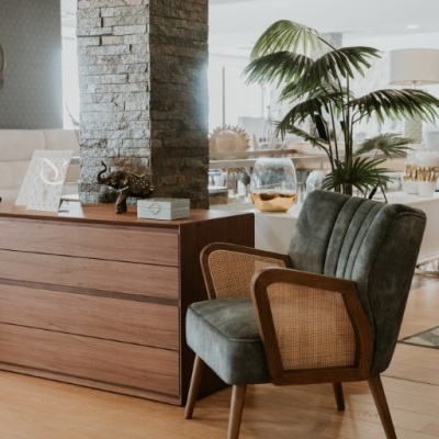 Cadeira estofada cinza com estrutura de madeira e fibras naturais ao lado de cómoda de madeira e coluna de pedra