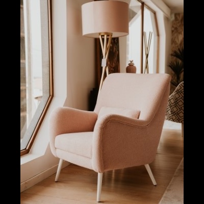 Poltrona rosa clara com almofada e lâmpada a pé junto a janela