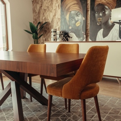 Mesa de jantar em madeira escura com cadeiras castanhas alaranjadas sobre tapete cinza com padrão geométrico.