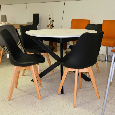 Mesa redonda branca com cadeiras pretas de madeira clara e base preta.