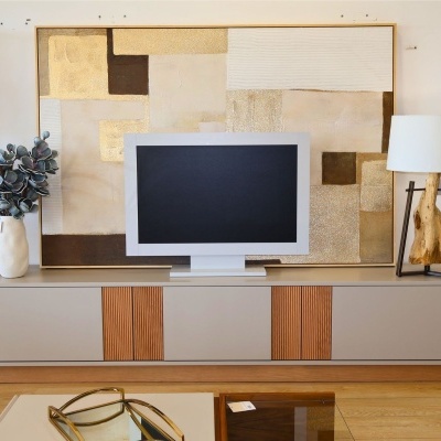 Móvel de TV com televisão, quadro abstrato, vaso com plantas e candeeiro de madeira