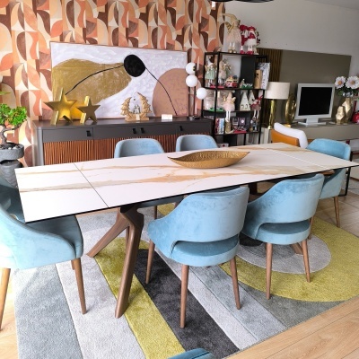 Mesa de jantar branca com cadeiras azuis em ambiente decorado com mobiliário moderno e tapete colorido.