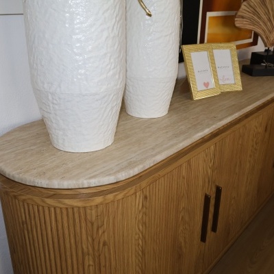 Aparador de madeira clara com tampo de mármore e vasos brancos.