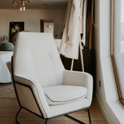 Cadeira creme estofada com estrutura preta perto de uma janela e cabideiro