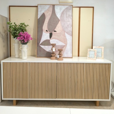Aparador branco com portas de ripas de madeira e decoração com vasos, flores, castiçais e quadros