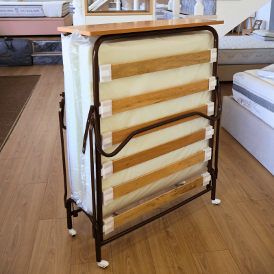 Cama dobrável com armação metálica castanho escuro e colchão branco numa loja de móveis