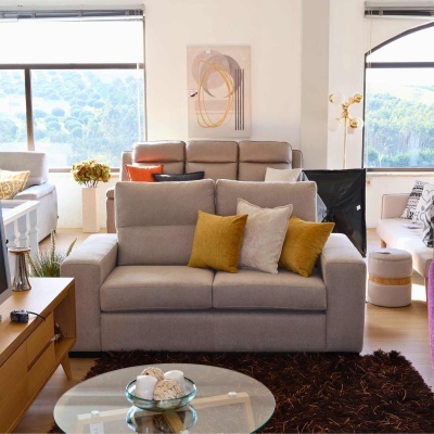 Sofá cinza claro com almofadas mostarda e bege numa sala moderna com tapete castanho.