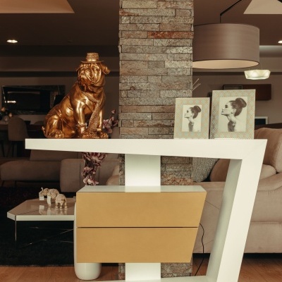 Mesa de consola branca em forma de Z com estátua dourada de cão e molduras de fotos em sala de estar