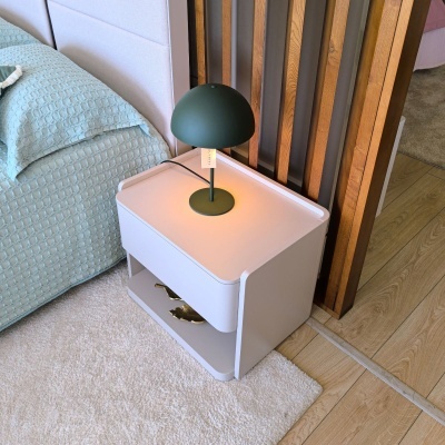 Mesa de cabeceira branca com candeeiro verde escuro ao lado de cama azul turquesa