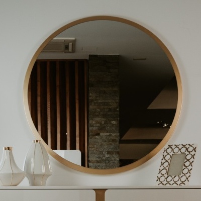 Espelho redondo com moldura de madeira clara sobre cómoda branca com vasos e moldura decorativa