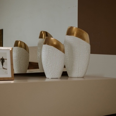 Dois vasos decorativos brancos com acabamento dourado sobre móvel com espelho ao fundo