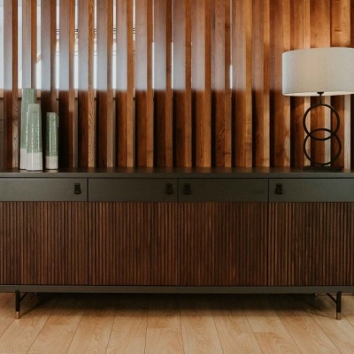 Aparador de madeira escura com planta, livros e abajur, parede de madeira rústica ao fundo