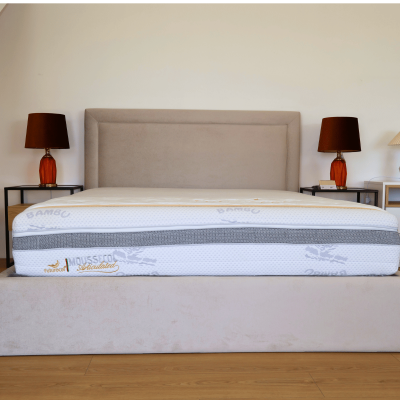 Cama estofada bege com colchão branco impresso, mesas de cabeceira com candeeiros laranja, chão de madeira