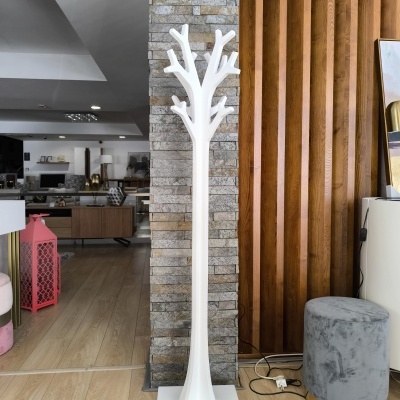 Cabideiro branco em forma de árvore contra parede de pedra e painel de madeira com pufe cinzento ao lado