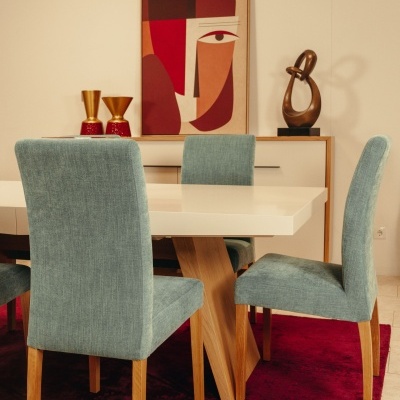 Mesa de jantar branca com cadeiras azul claro sobre tapete vermelho, móvel branco com decoração e quadro abstrato ao fundo.