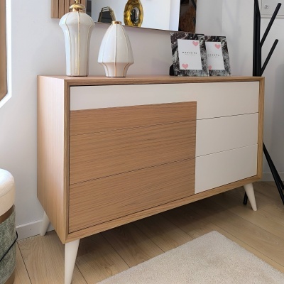 Cómoda moderna em madeira clara com gavetas em madeira natural e branco, decorada com vasos e quadros pequenos.