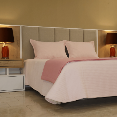 Quarto com cama de casal com roupa de cama rosa e mesas de cabeceira com abajures vermelhos