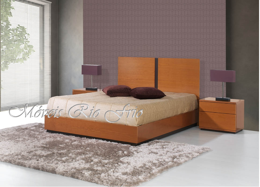 Quarto com cama de madeira clara, cabeceira em dois painéis, duas mesinhas de cabeceira e candeeiros roxos