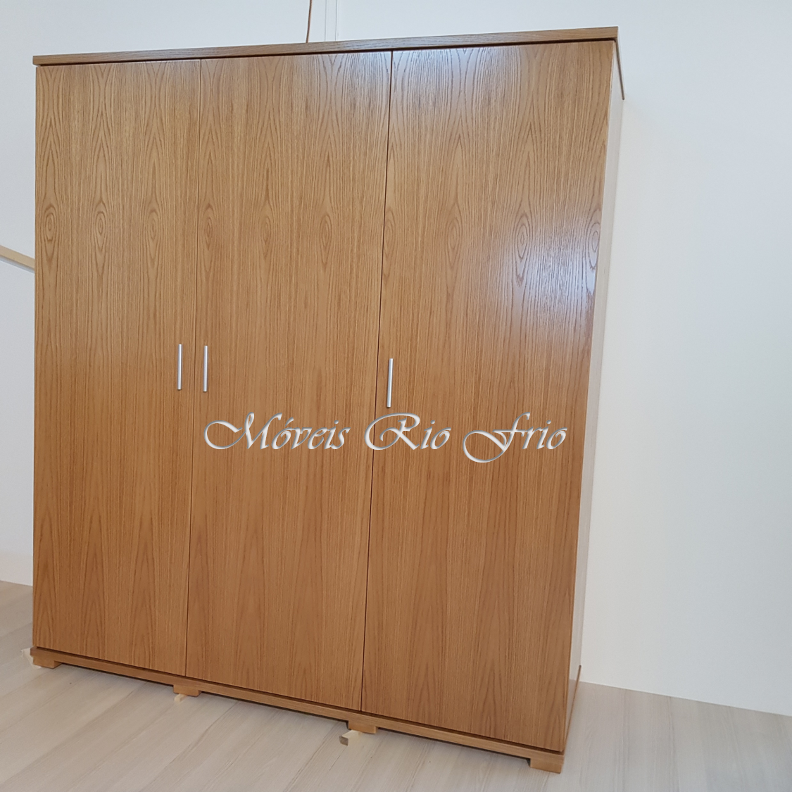 Armário de madeira clara com três portas e puxadores metálicos