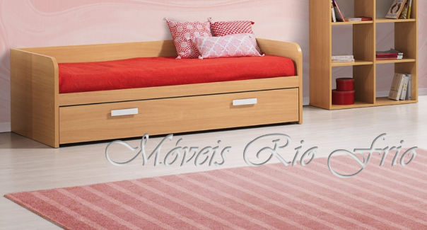 Cama individual em madeira clara com colchão vermelho e almofadas decorativas, gaveta e tapete rosa listrado