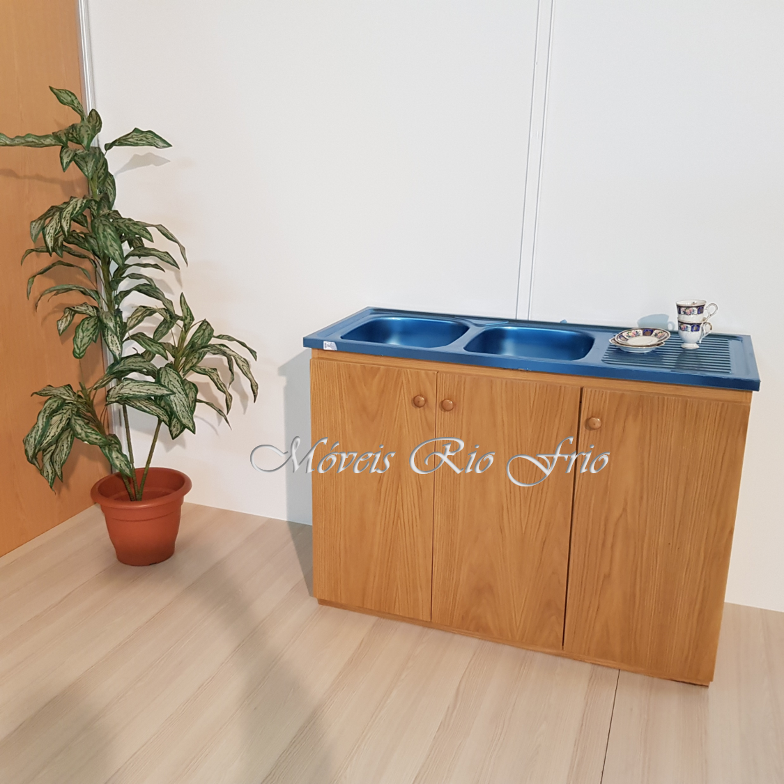 Bancada de cozinha em madeira clara com lava-louça azul e planta em vaso