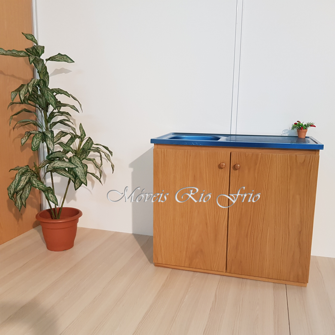 Móvel de cozinha em madeira clara com tampo azul e pia ao lado de planta em vaso
