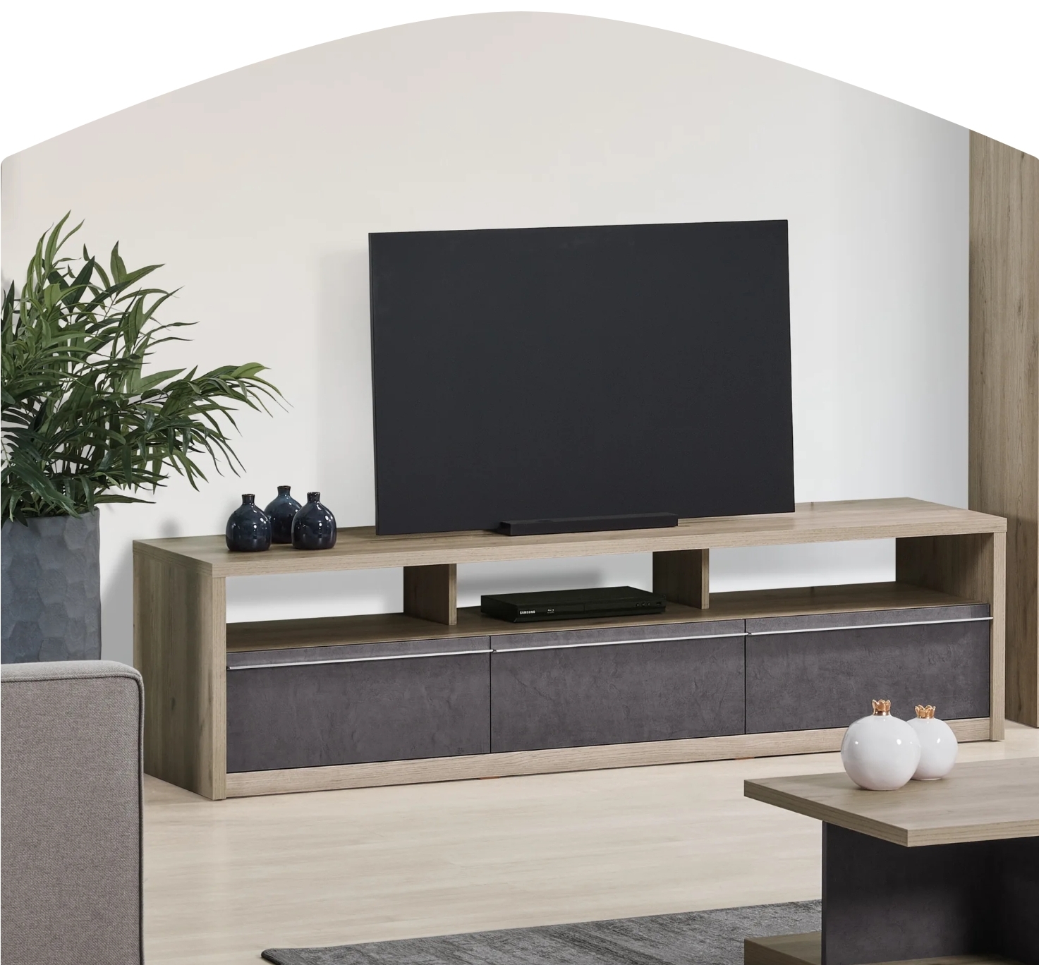 Móvel TV madeira clara com gavetas cinzentas, televisão preta, vasos e planta em sala clara