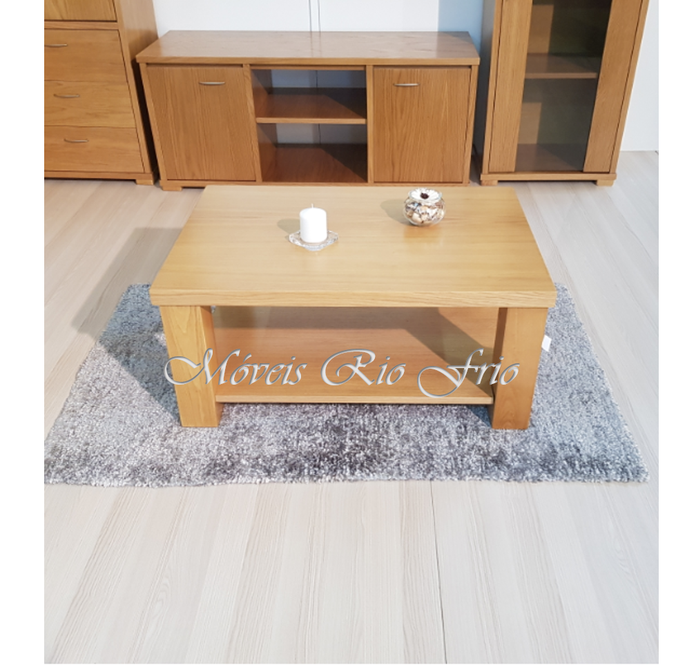 Mesa de centro de madeira clara com vela e vaso em cima, sobre tapete cinza, com móveis de madeira ao fundo