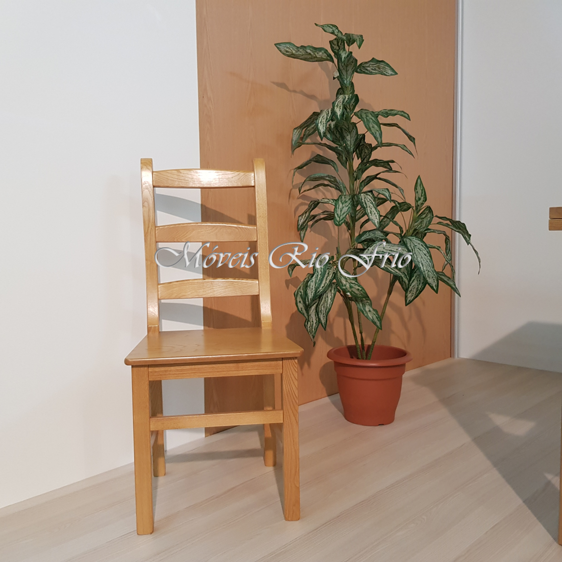 Cadeira de madeira clara ao lado de planta verde em vaso terracota