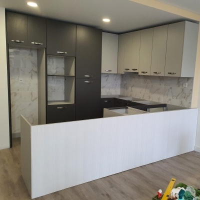 Cozinha moderna com armários cinza escuro e claro, azulejo efeito mármore e bancada branca em fase de montagem.