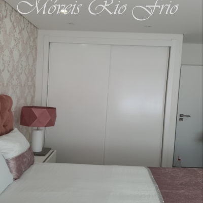 Quarto com cama branca e rosa, armário de portas de correr brancas, abajur rosa e papel de parede padrão