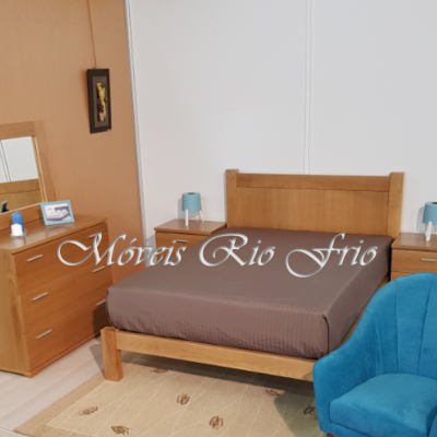 Quarto com cama de madeira, mesas de cabeceira, cómoda com espelho, poltrona azul e tapete bege