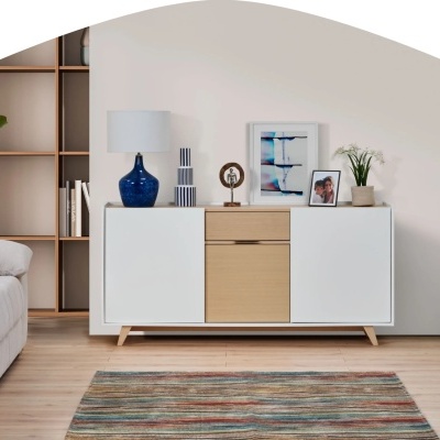 Aparador branco com portas e gaveta em madeira clara decorado com objetos e quadro numa sala com estante e sofá claro